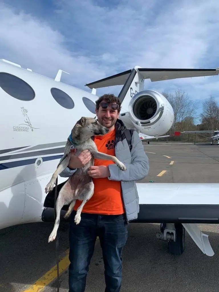 private jet man standing holding a dog under his arm